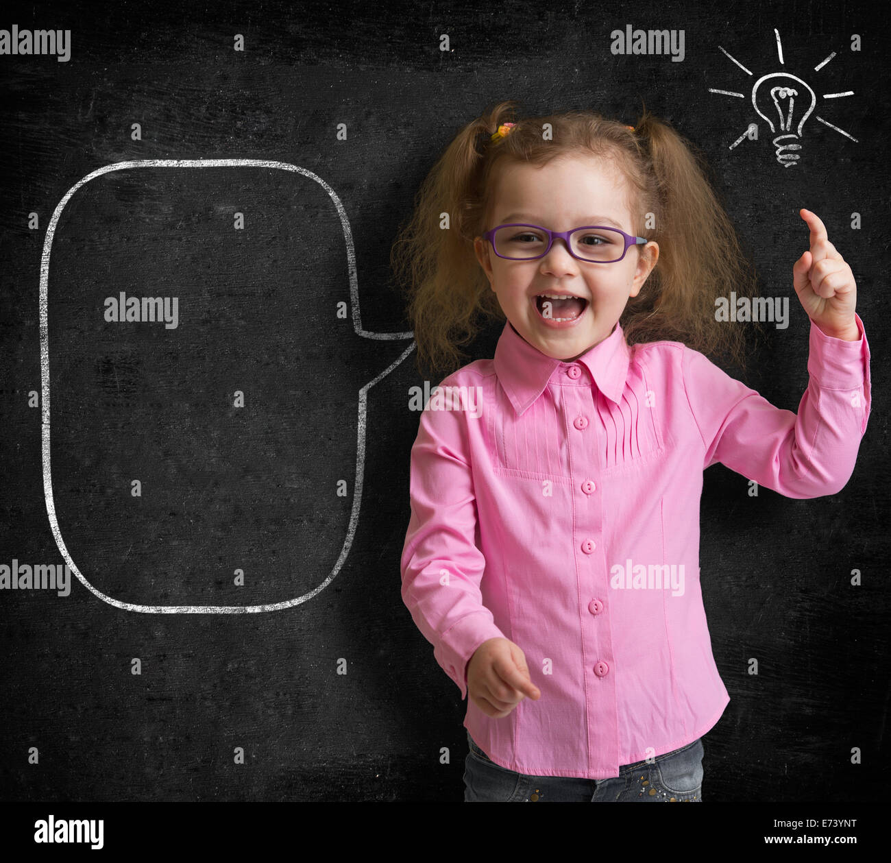 Happy kid girl in glasses with bright idea standing near school blackboard in classroom Stock Photo