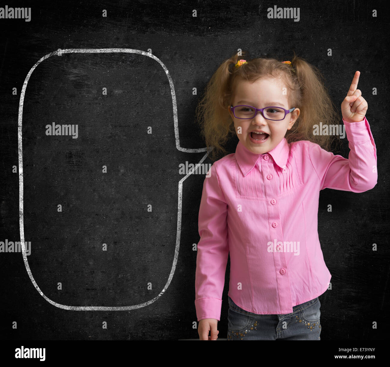 Funny child in eyeglasses standing near school chalkboard  as a teacher with blank speech bubble scetch. Stock Photo