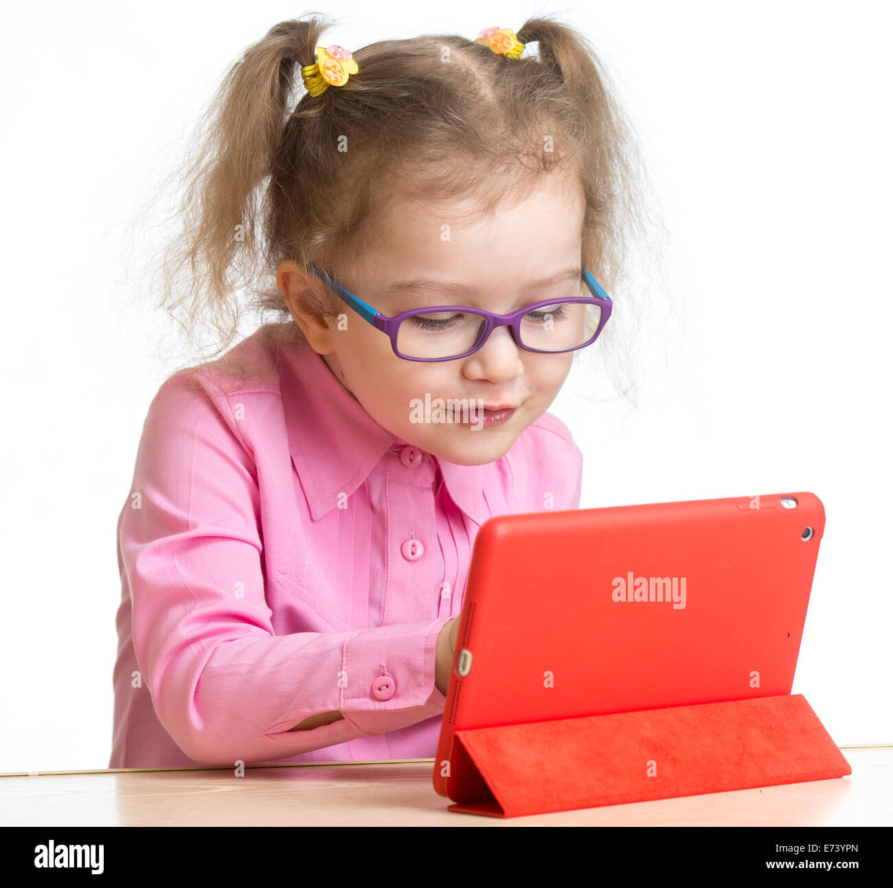 kid in glasses looking at mini tablet pc screen sitting at table Stock Photo