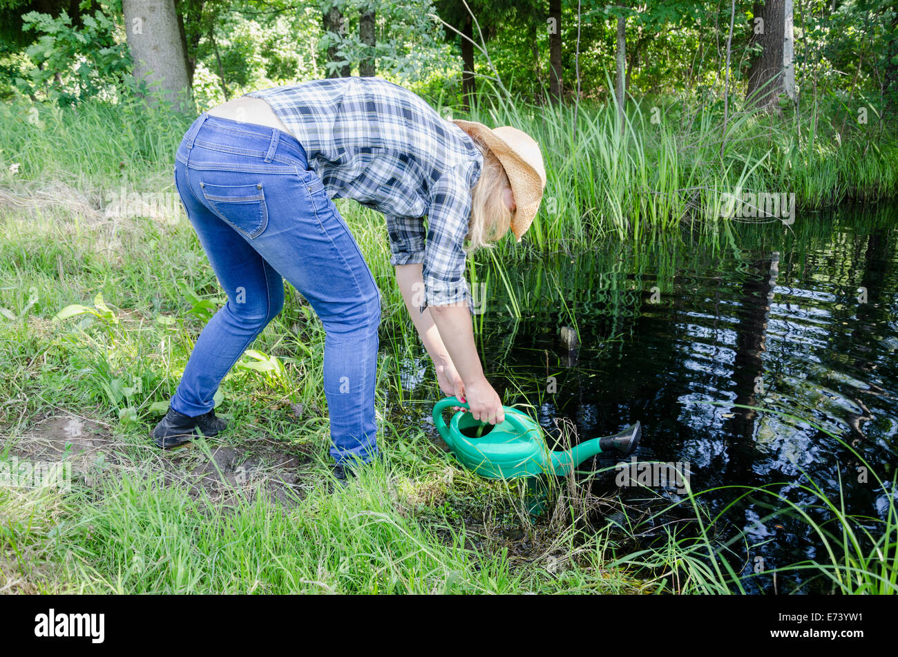 gardener girl draw water from pond with watering-can. Stock Photo
