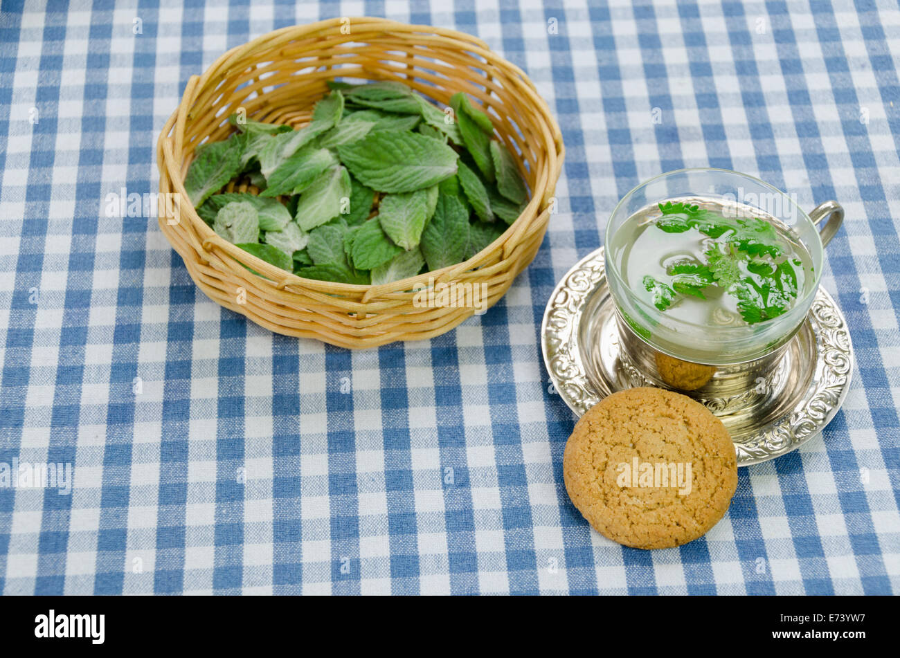 fresh healthy mint tea prepared in cup and dietary oatmeal cookie on checkered tablecloth Stock Photo
