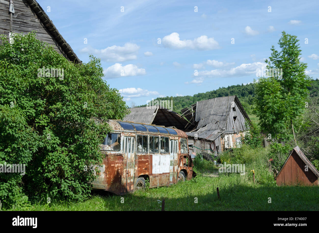 old rusty broken passenger bus stand along country rotten house in summer time Stock Photo