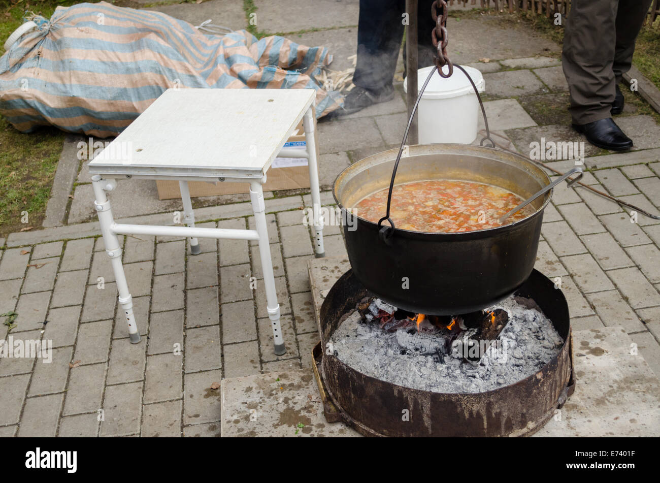 big black metal old pot full of rustic vegetable soup on an open fire outdoors Stock Photo