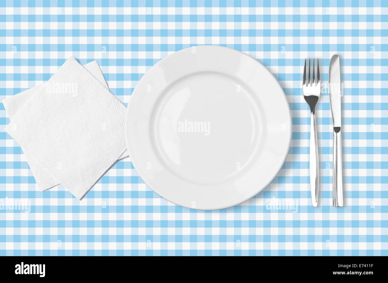plate, fork, knife and napkin over blue checked fabric tablecloth top view Stock Photo
