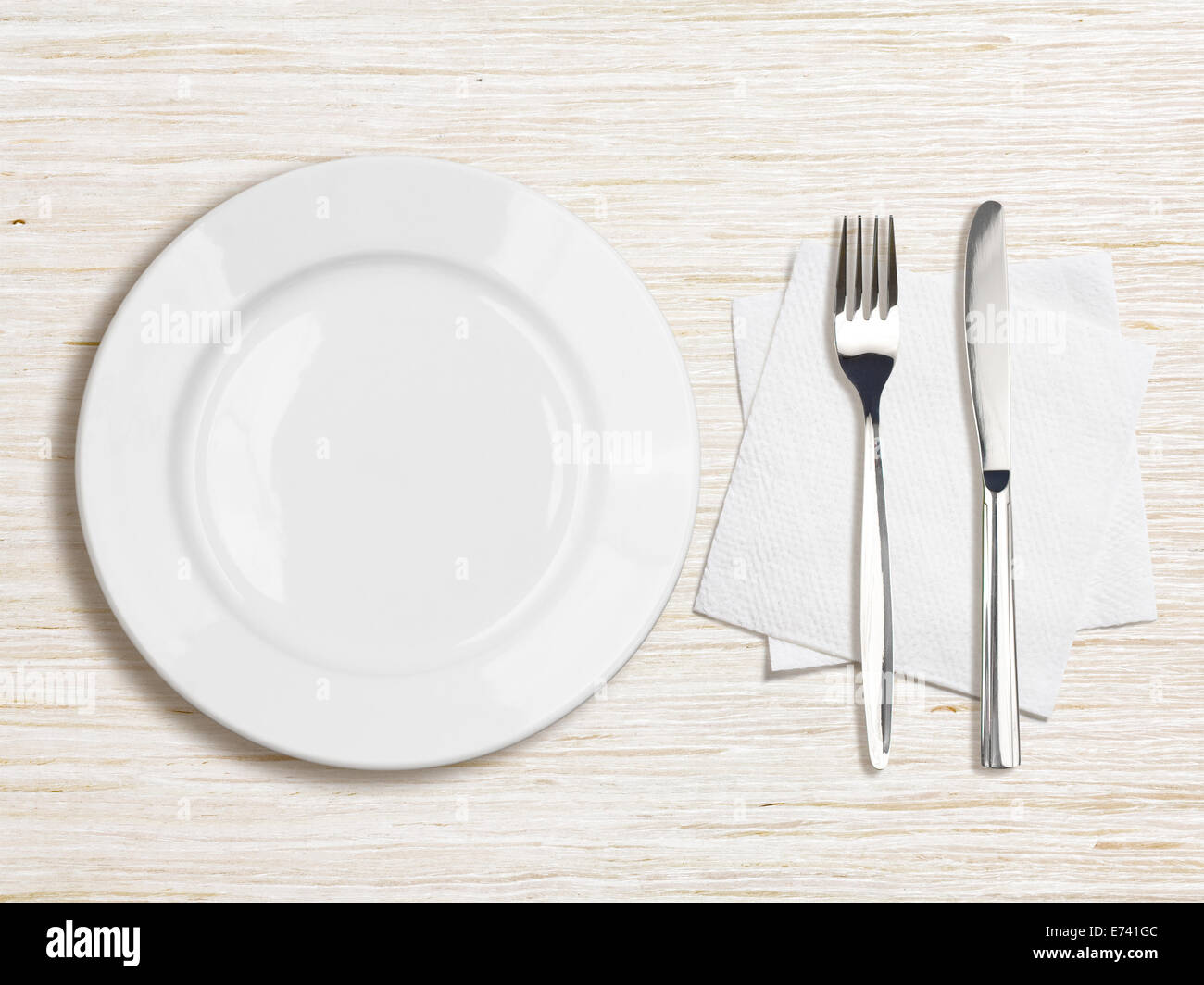 white plate, knife, fork and napkin top view on wooden table Stock Photo