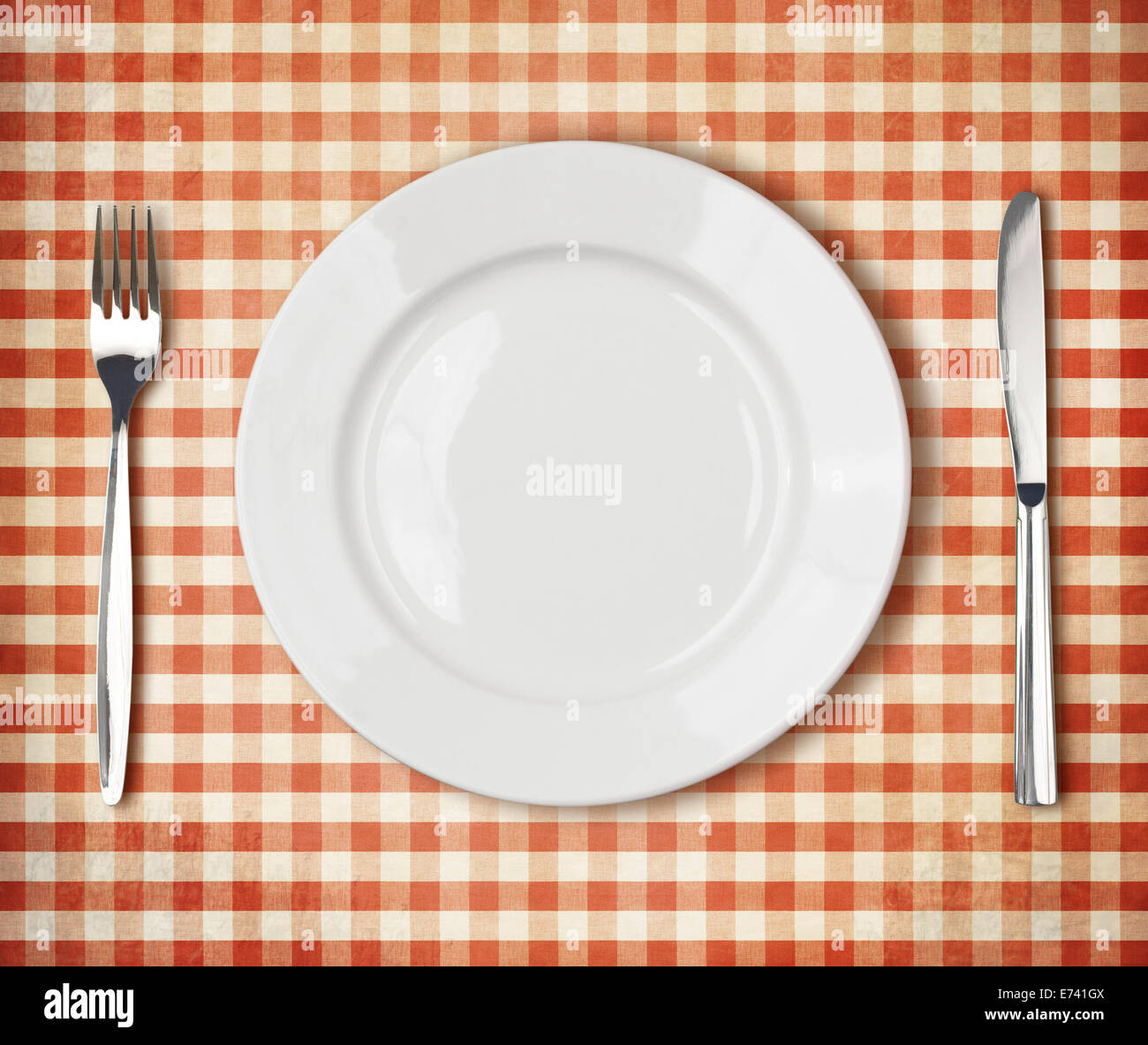 white plate, fork, knife top view over old red picnic tablecloth Stock Photo