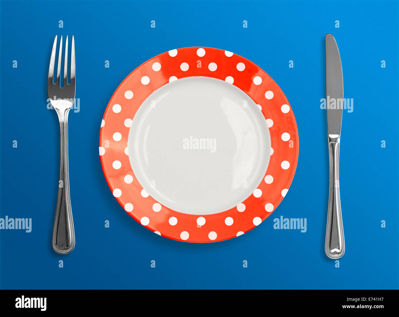 polka dot red plate with fork and knife top view on blue background Stock Photo