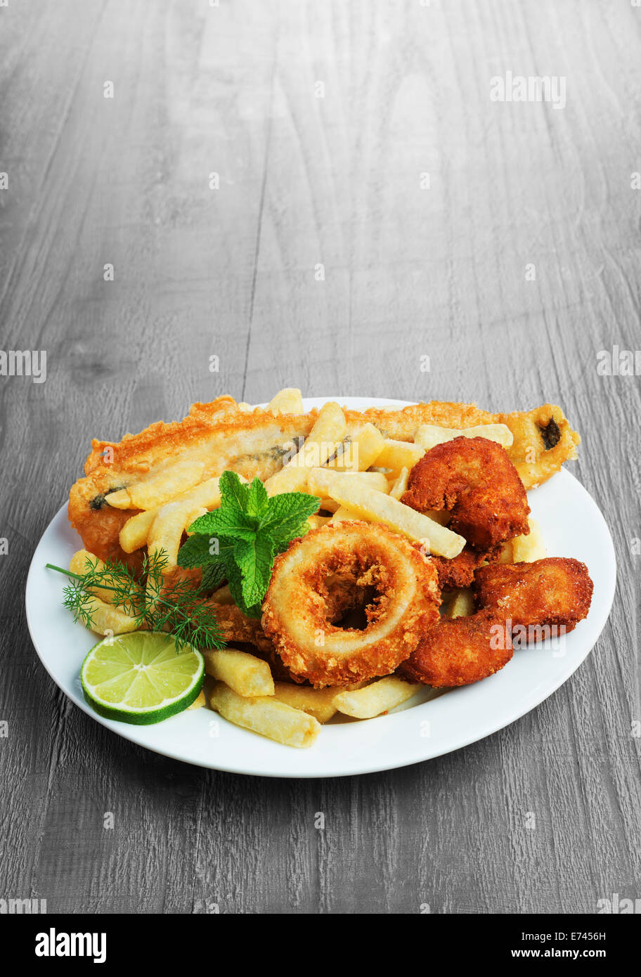 Seafood dish with crumbed fish,calamari,prawn and potato chips on vintage table Stock Photo