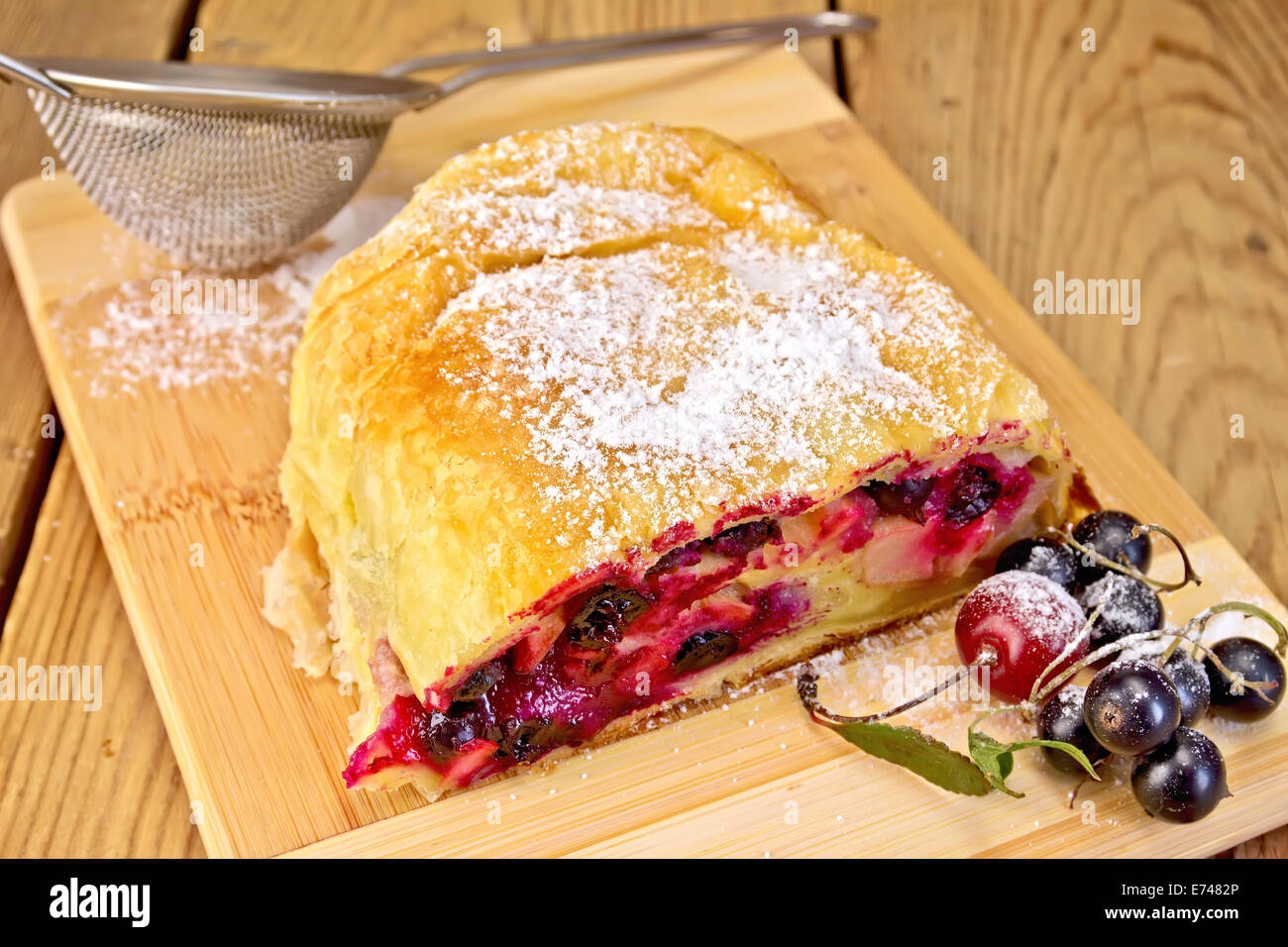 Strudel with black currant and cherry, metal sieve, powdered sugar on a wooden boards background Stock Photo