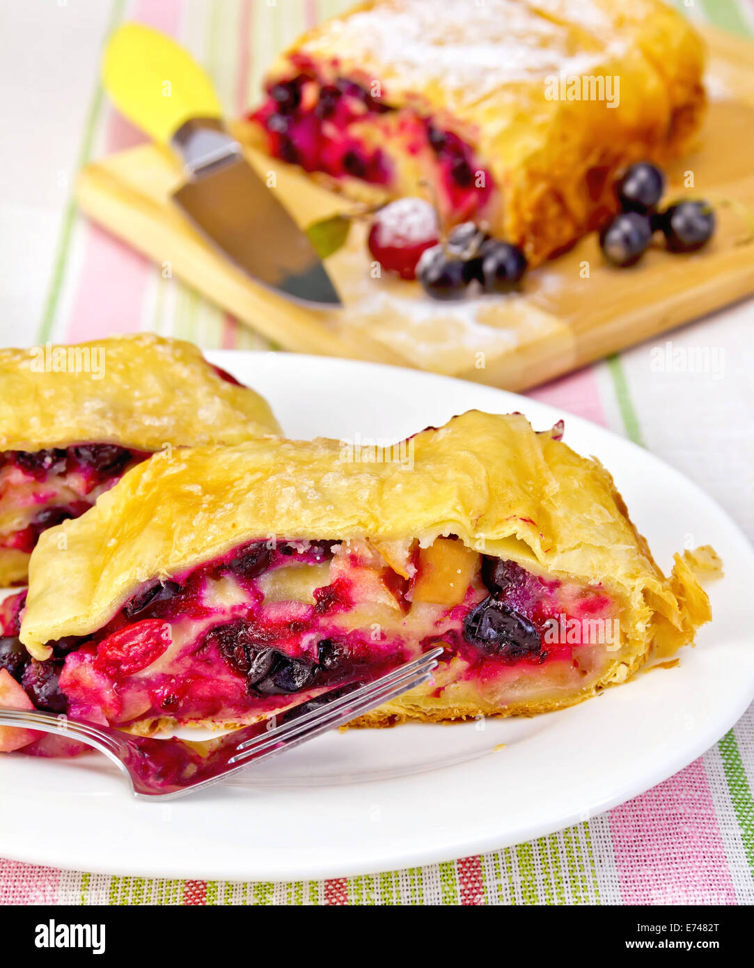 Strudel with black currant and cherry on a plate with fork, knife on background linen tablecloth Stock Photo