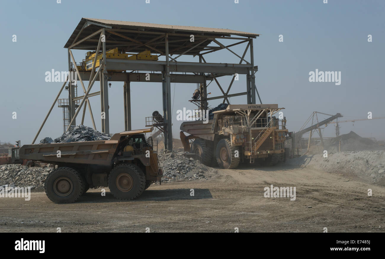 Caterpillar and Hitachi haul trucks wait at the crusher of a large open cast African copper mine. Stock Photo