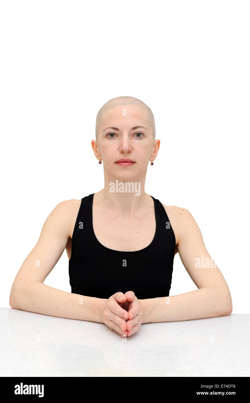 Bald woman in black sleeveless shirt, sitting calm at a table, palms joined. Isolated with clipping path Stock Photo
