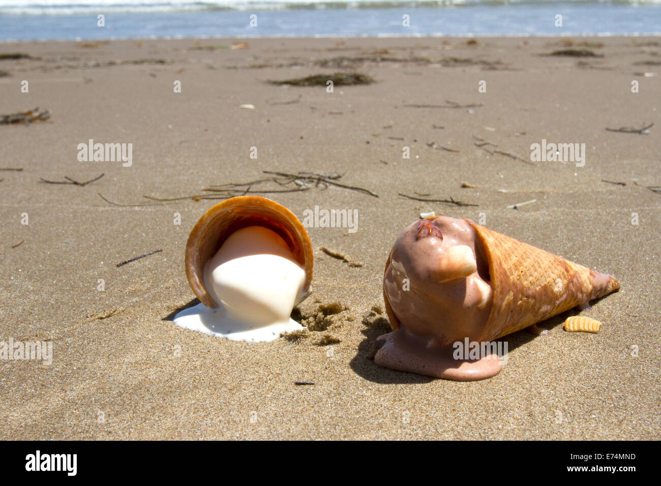 Chocolate and vanilla ice cream cones melting on deserted beach Stock Photo