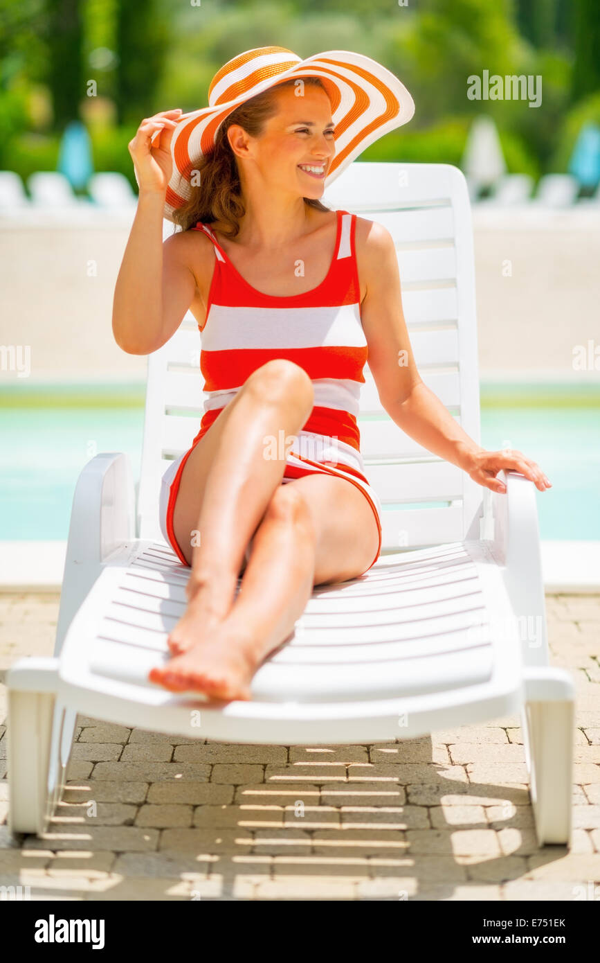 Smiling young woman in hat sitting on sunbed Stock Photo - Alamy