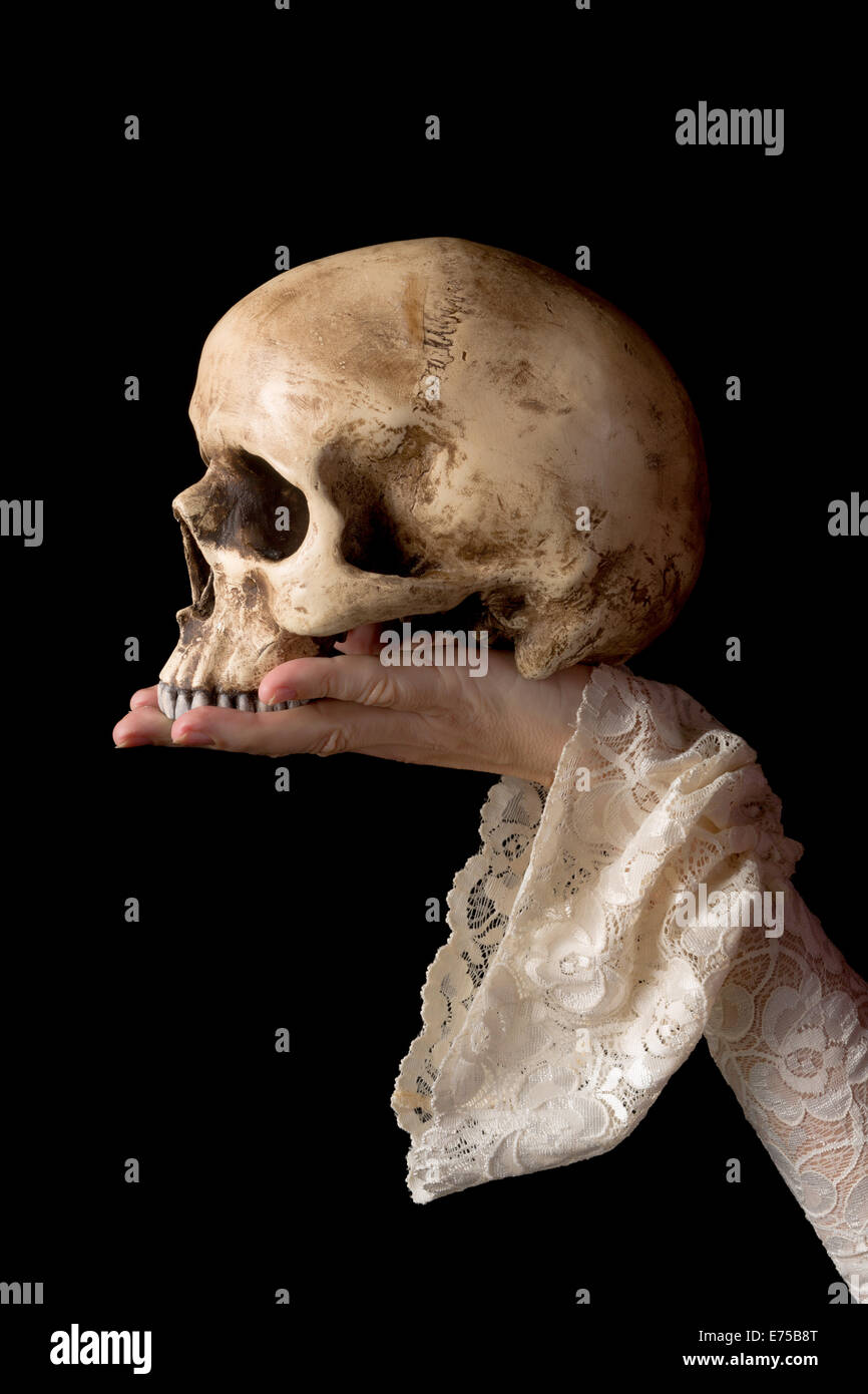Creepy human skull held by a female hand wearing antique lace sleeves Stock Photo