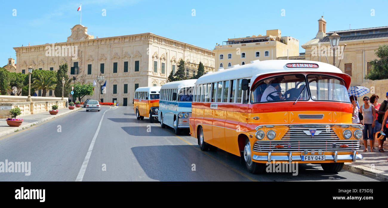 Three old restored Maltese buses delivering passengers to a bus stop close to The Maltese Prime Ministers offices seen beyond Stock Photo