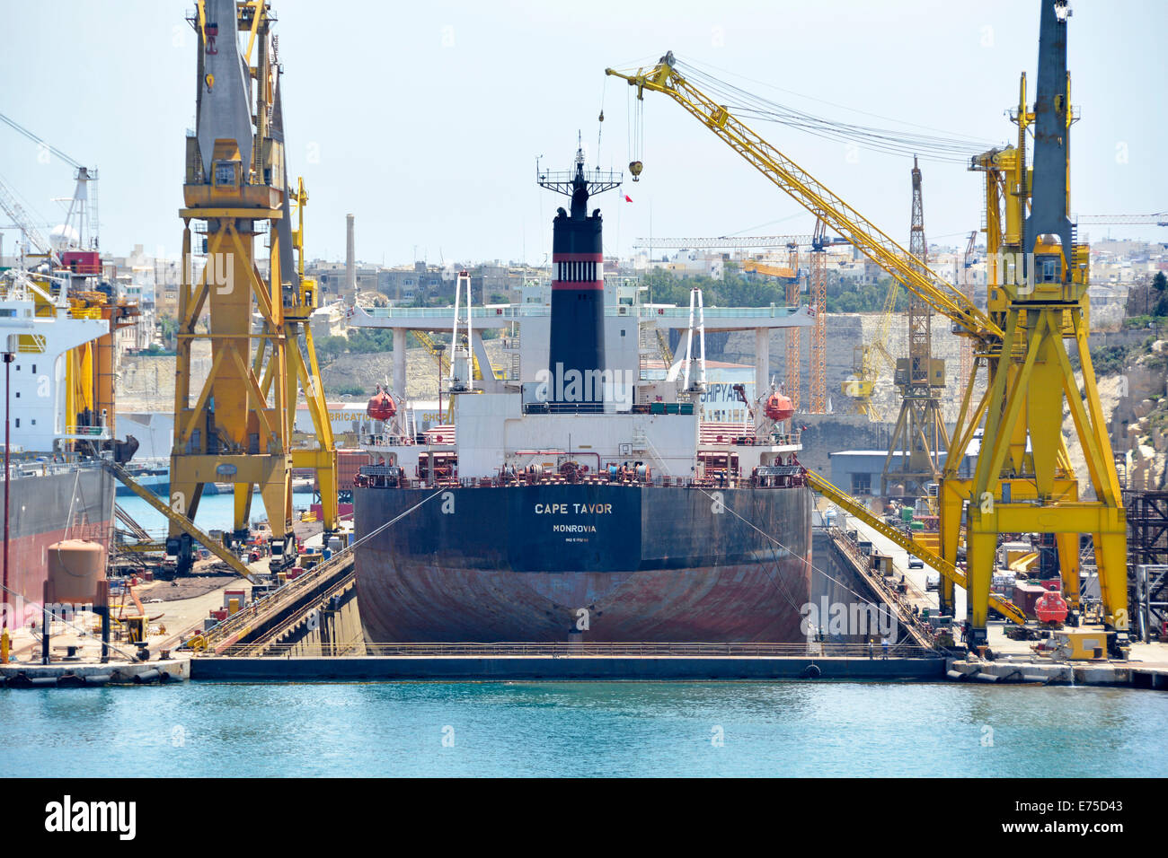 People at waters edge dwarfed by close up stern of Bulk carrier freighter Cape Tavor dry dock & shipyard cranes Grand Harbour Port Valletta Malta EU Stock Photo
