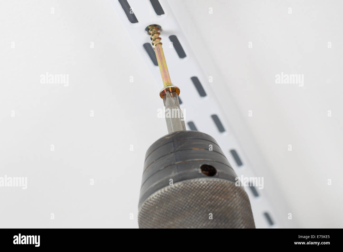 Closeup of power screwdriver putting screw into support bracket on wall with focus on head of screw Stock Photo