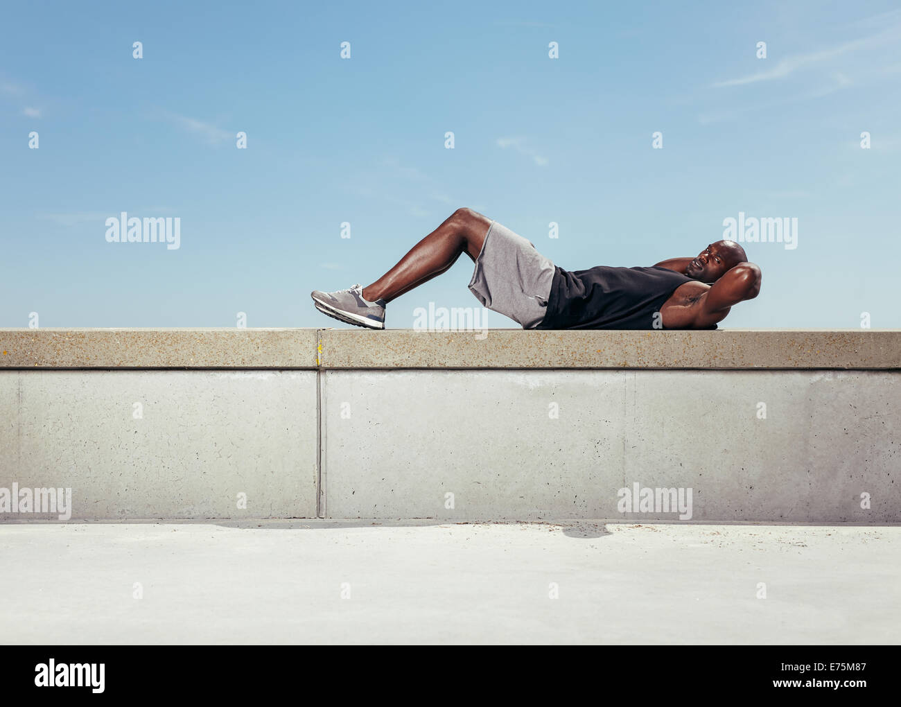 Muscular young man doing sit-ups looking at camera. African guy exercising outdoors with copy space. Stock Photo