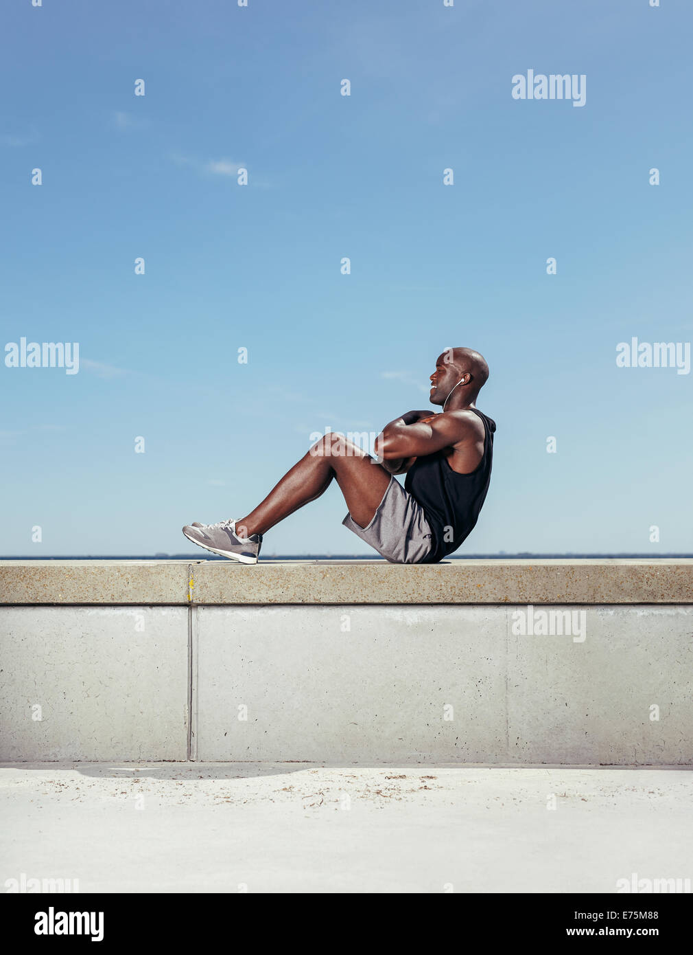 Side view of fit young man exercising outdoors. Muscular young man doing sit-ups against sky. Stock Photo