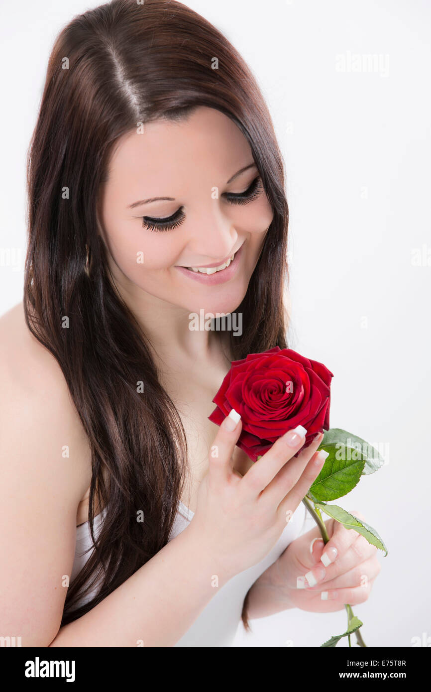 Young woman smiling at a red rose Stock Photo