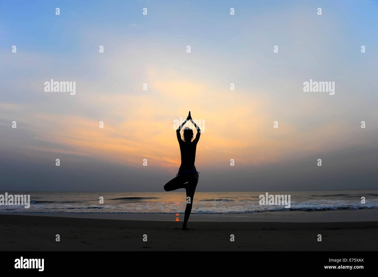 Woman doing yoga on a beach at dusk, Kerala, India Stock Photo