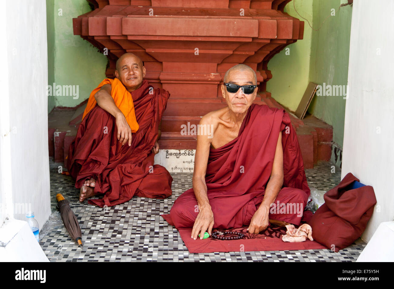 Buddhist monks sitting in front of a place of worship in a temple, one of them wearing Ray Ban sunglasses, Yangon, Myanmar Stock Photo