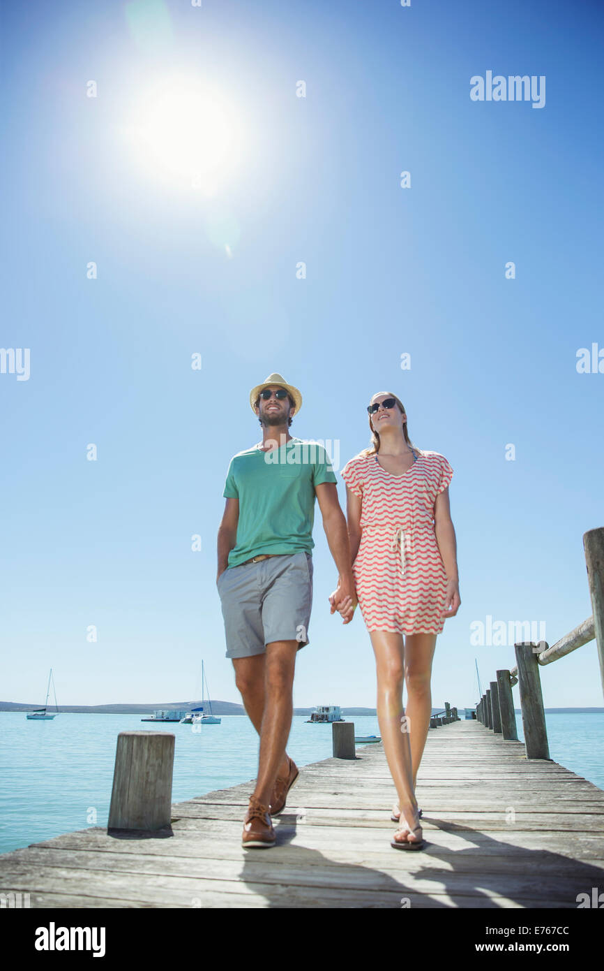 Couple holding hands walking along wooden dock Stock Photo