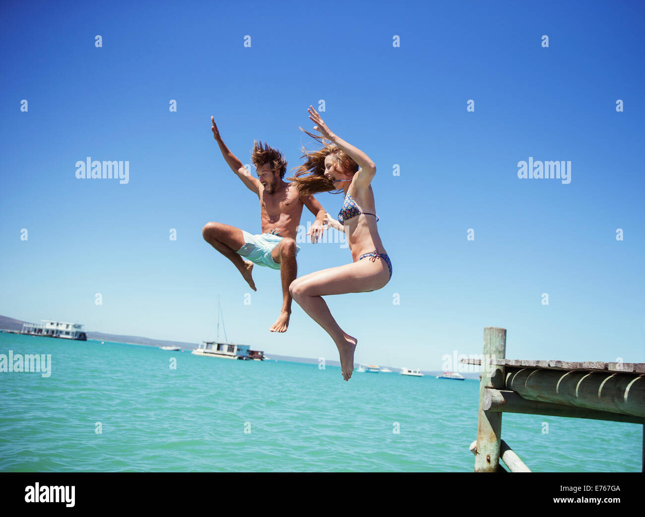 Couple jumping off wooden dock together Stock Photo