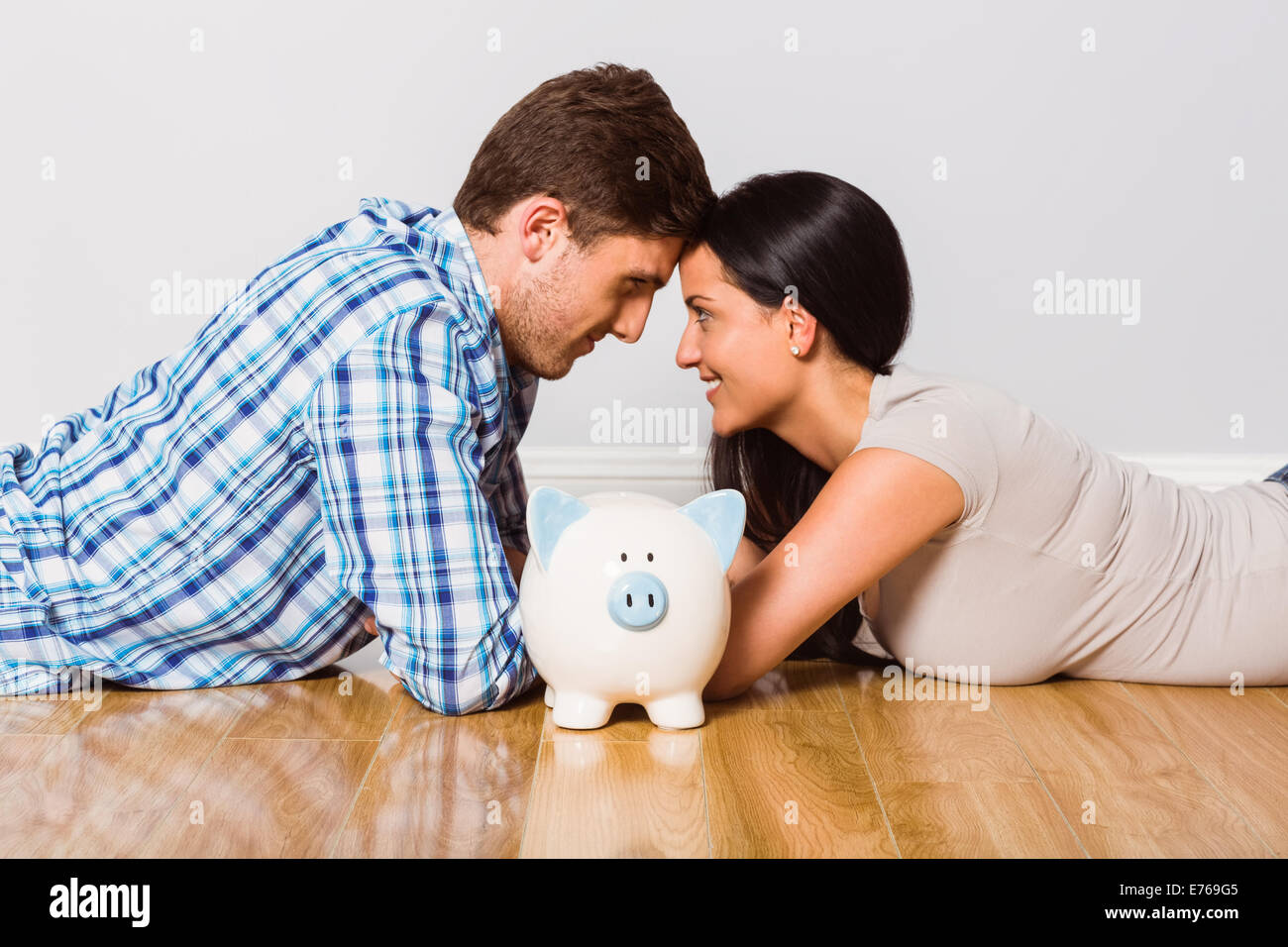 Young couple lying on floor smiling with piggy bank Stock Photo - Alamy