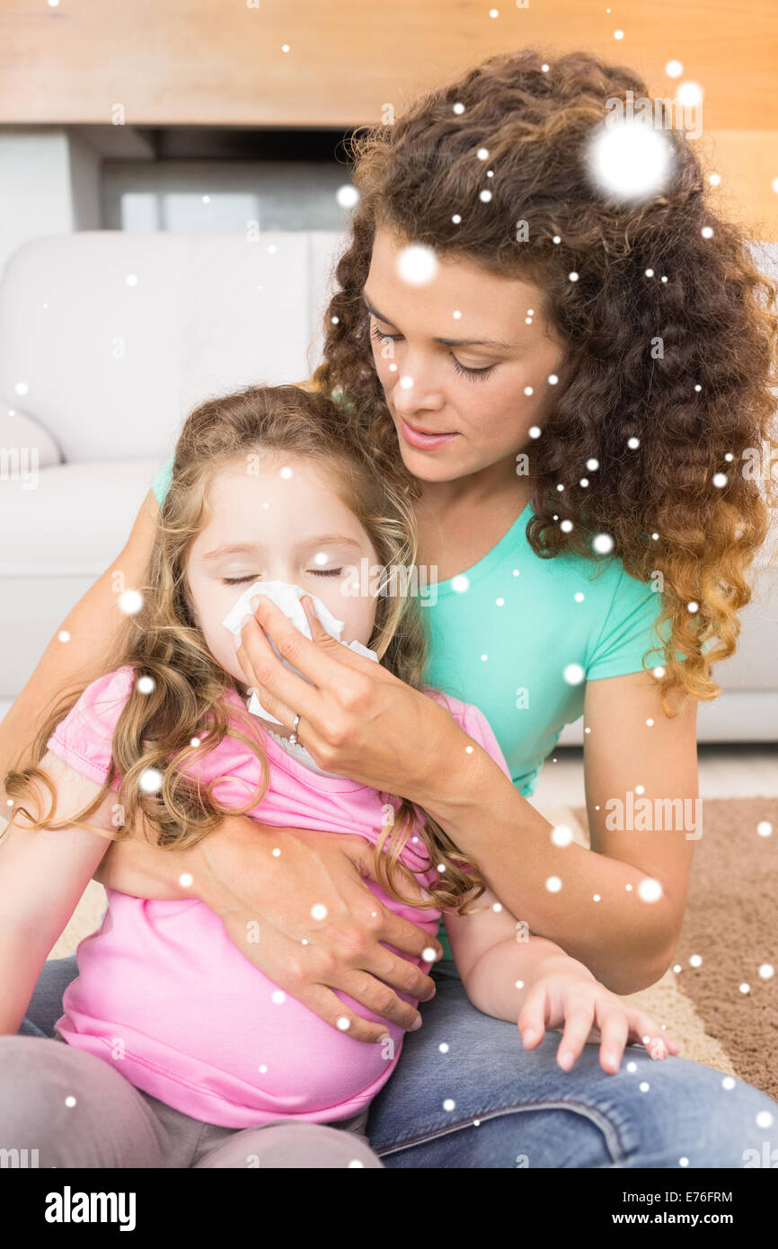 Composite image of caring mother helping her little daughter blow her nose Stock Photo