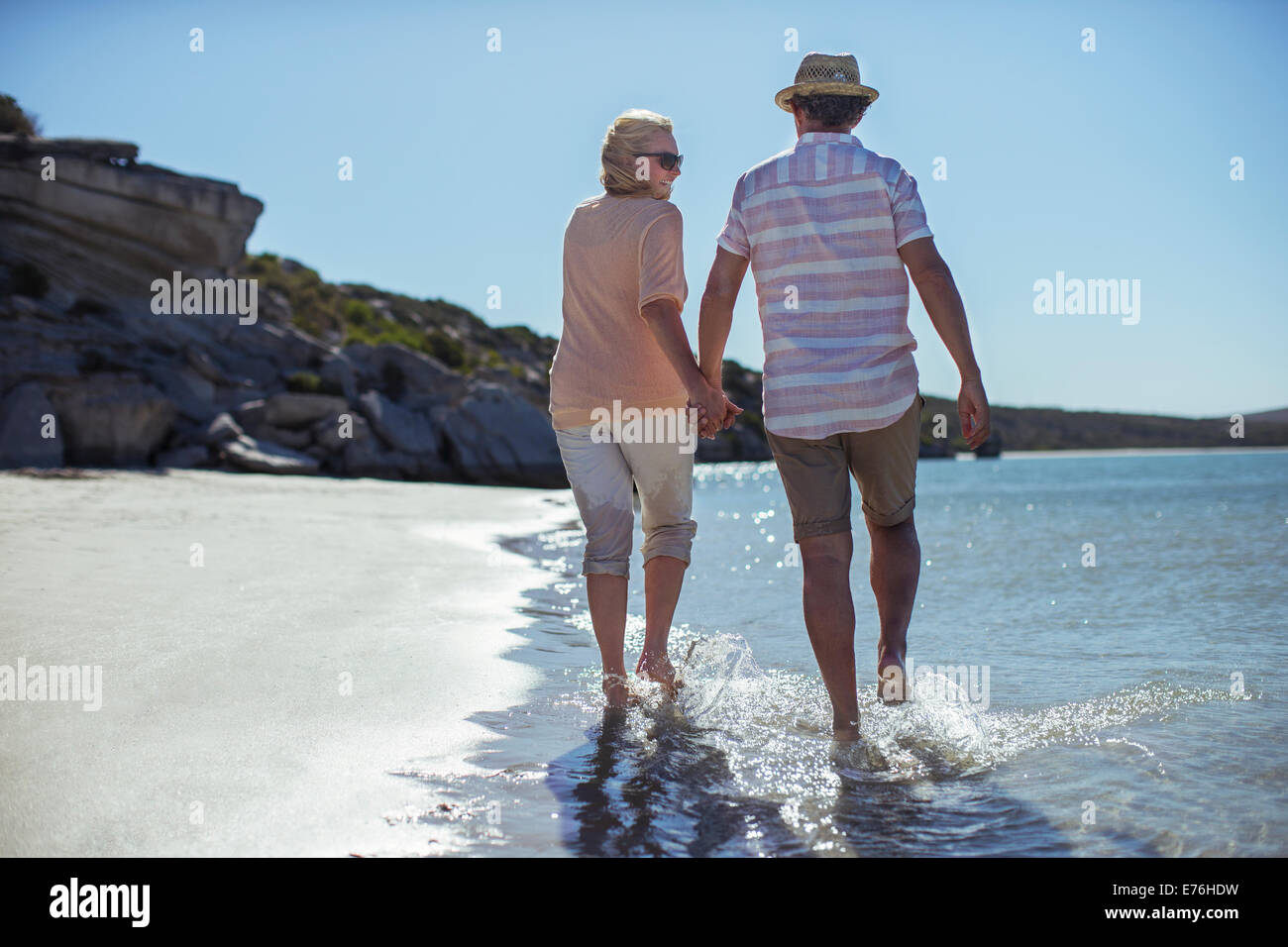 Couple holding hands walking along shore Stock Photo