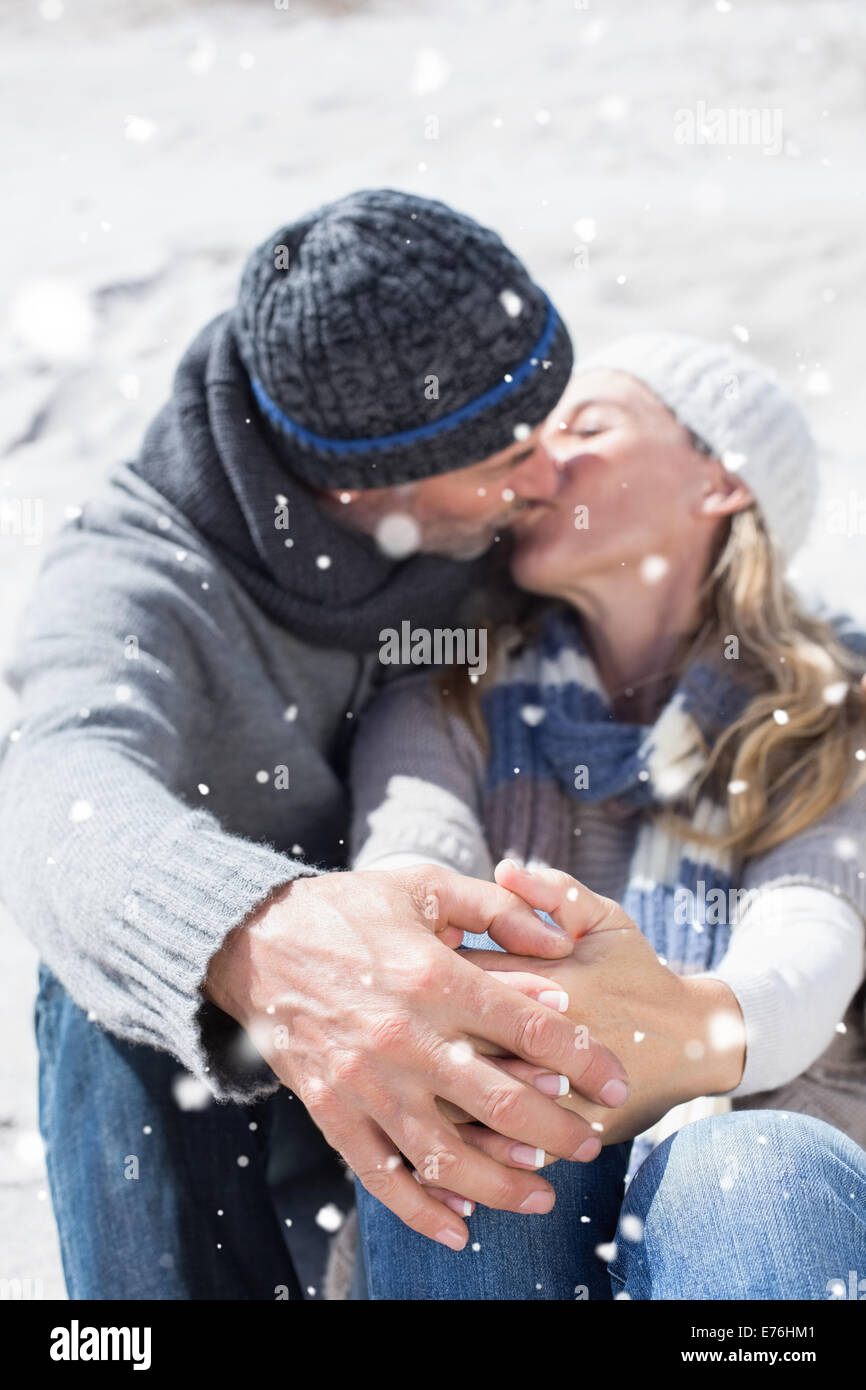 Composite image of attractive couple kissing on the beach in warm clothing Stock Photo