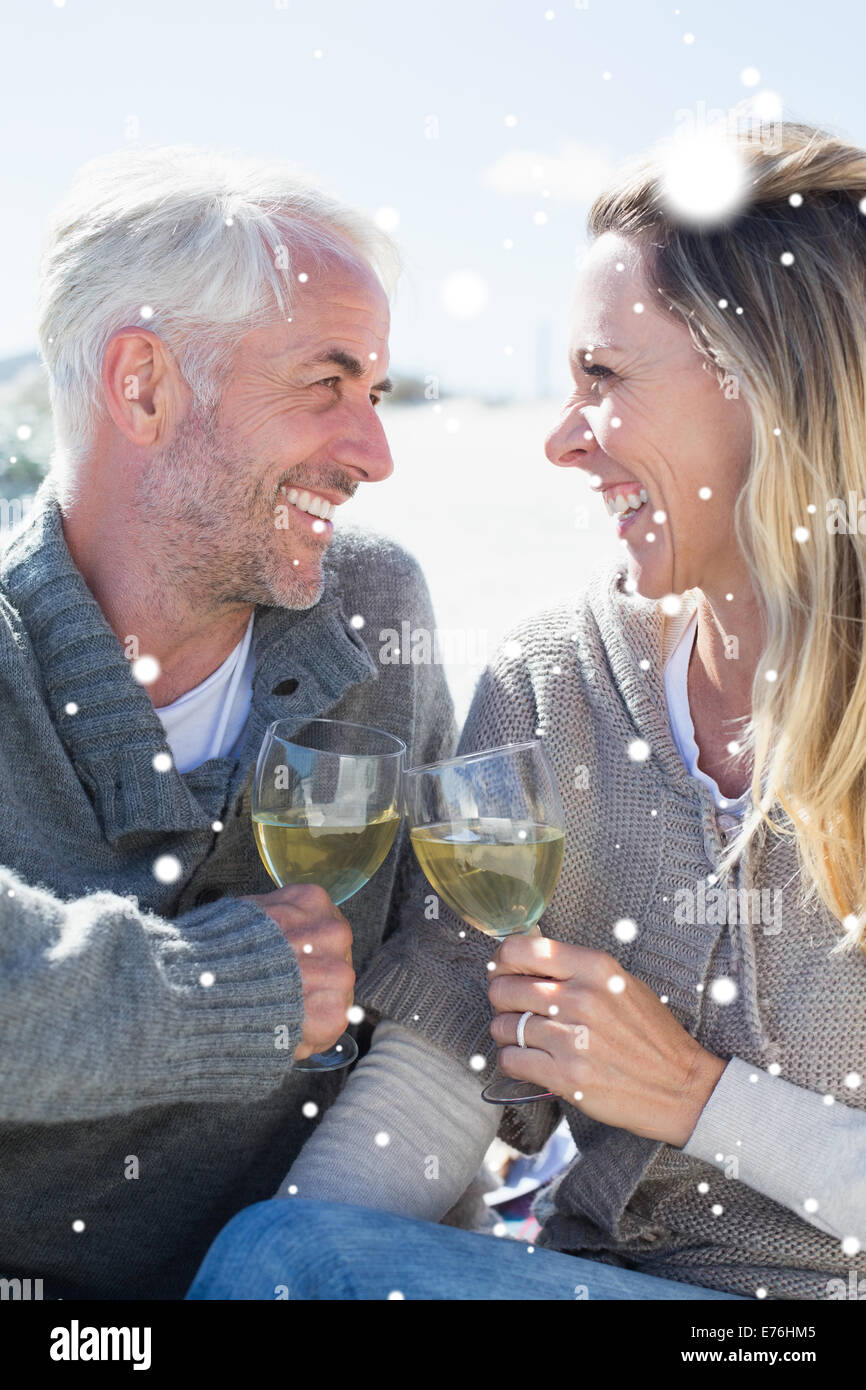 Composite image of couple enjoying white wine on picnic at the beach