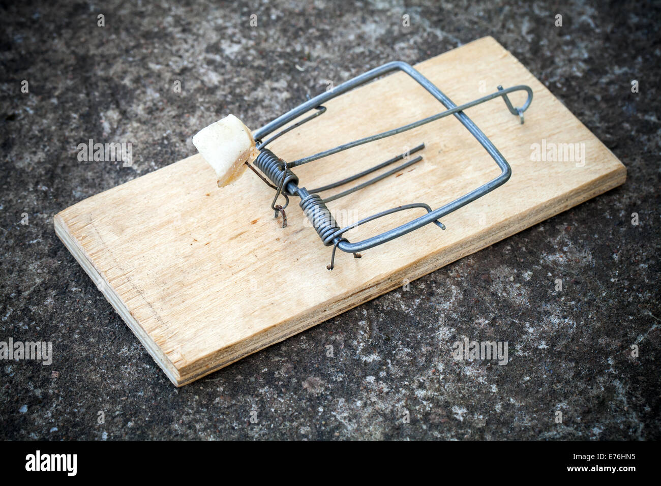 Old mousetrap with fat bait stands on concrete floor Stock Photo