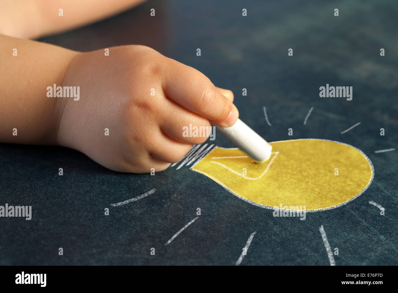 Macro close up of infant hand drawing a yellow bulb on blackboard. Stock Photo