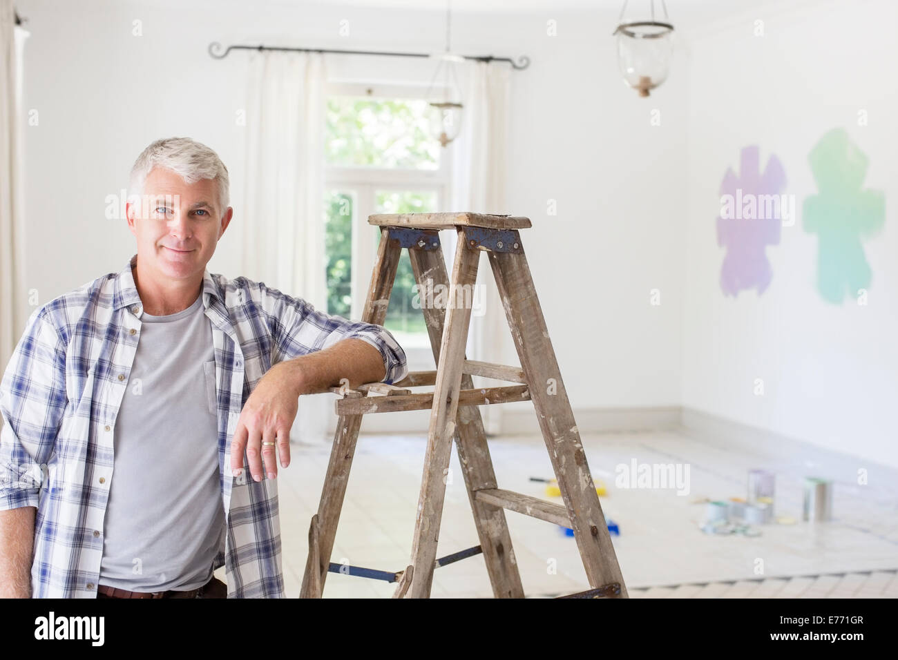 Older man smiling near ladder in livingroom Stock Photo