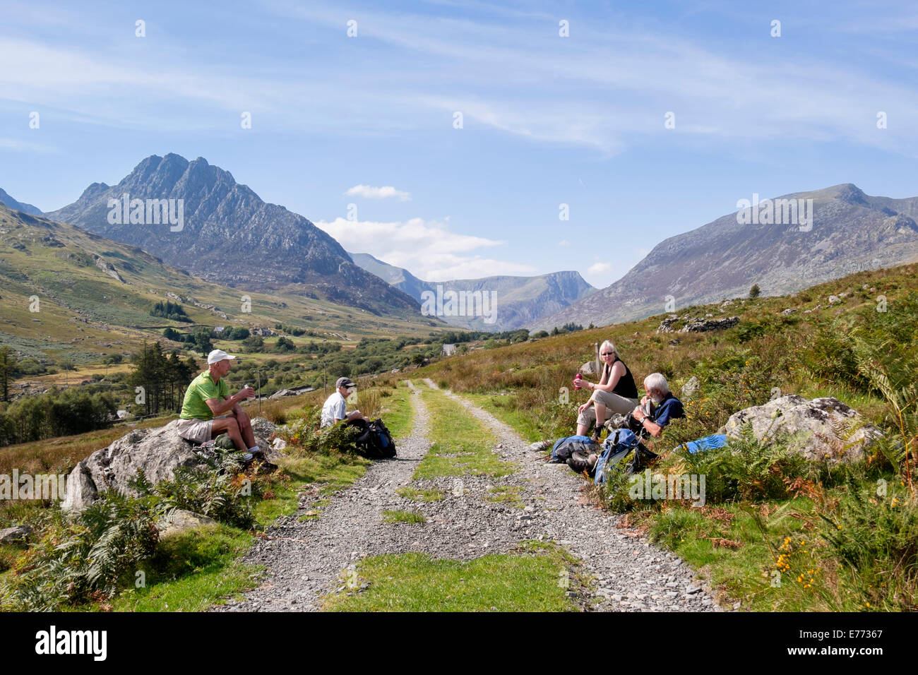 Walkers having a break resting by a track in Ogwen Valley with view to Mount Tryfan in Snowdonia National Park mountains. Ogwen Valley North Wales UK Stock Photo