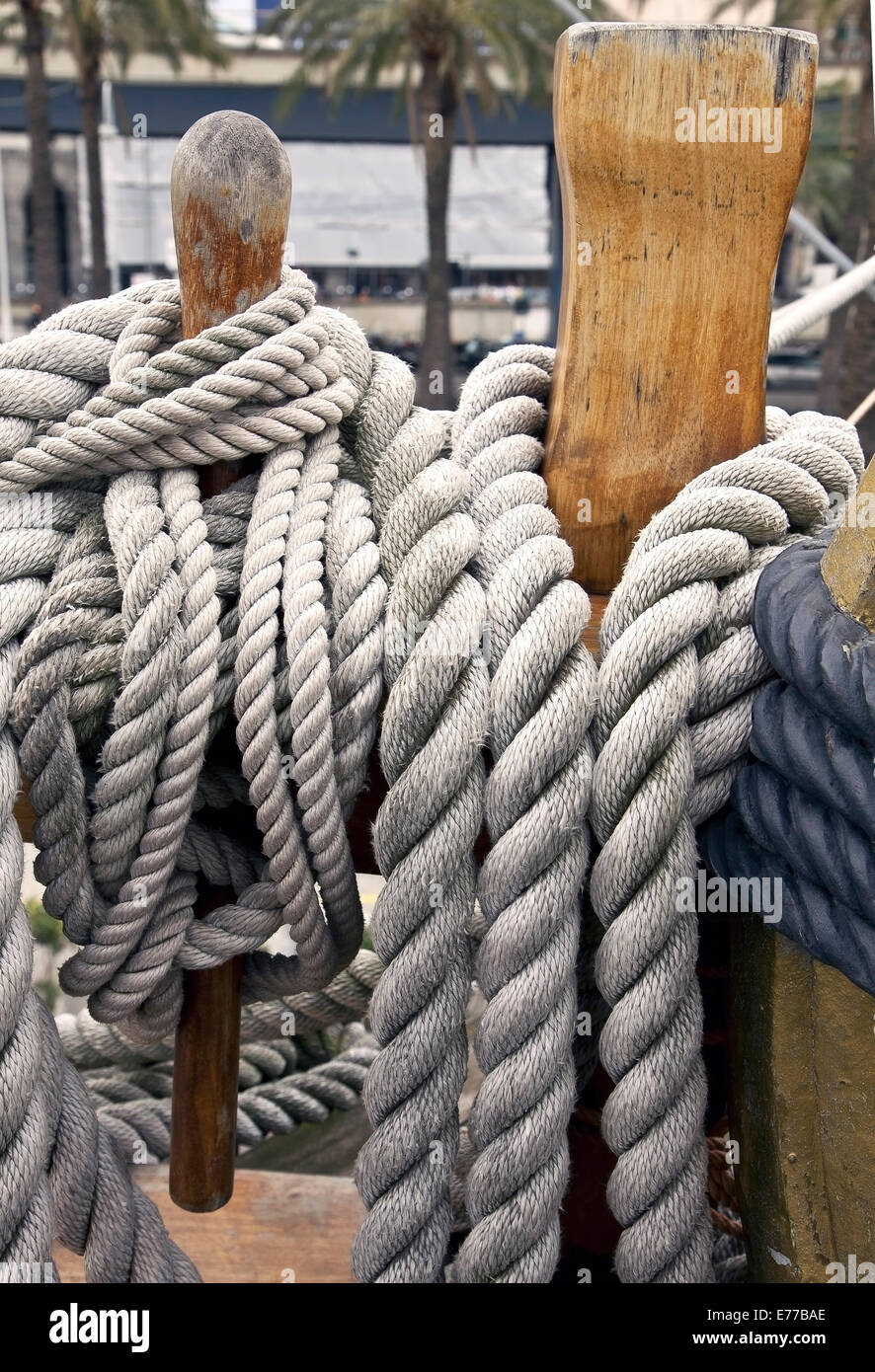 ropes of different sizes fastened around wooden cleats on a yacht wooden deck Stock Photo