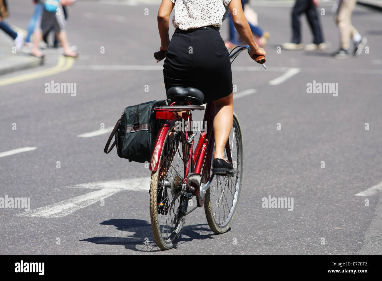 Rear view of a female riding a cycle in London. Pedestrians crossing the road in the distance. Stock Photo