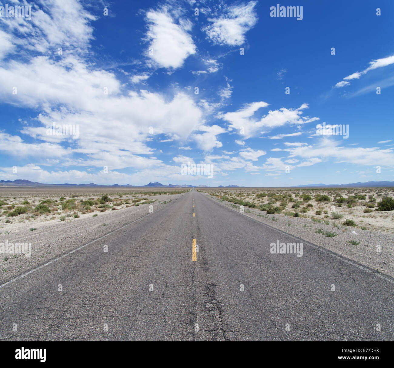 an empty desert road cuts across Nevada to the horizon under a partly cloudy blue sky Stock Photo