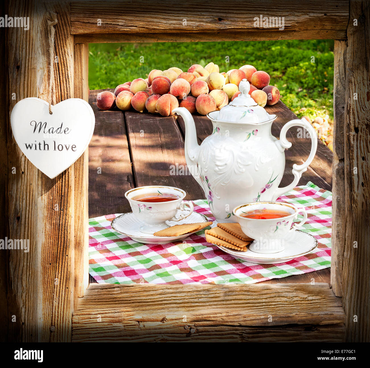 Tea set in garden in wooden frame with heart. Stock Photo