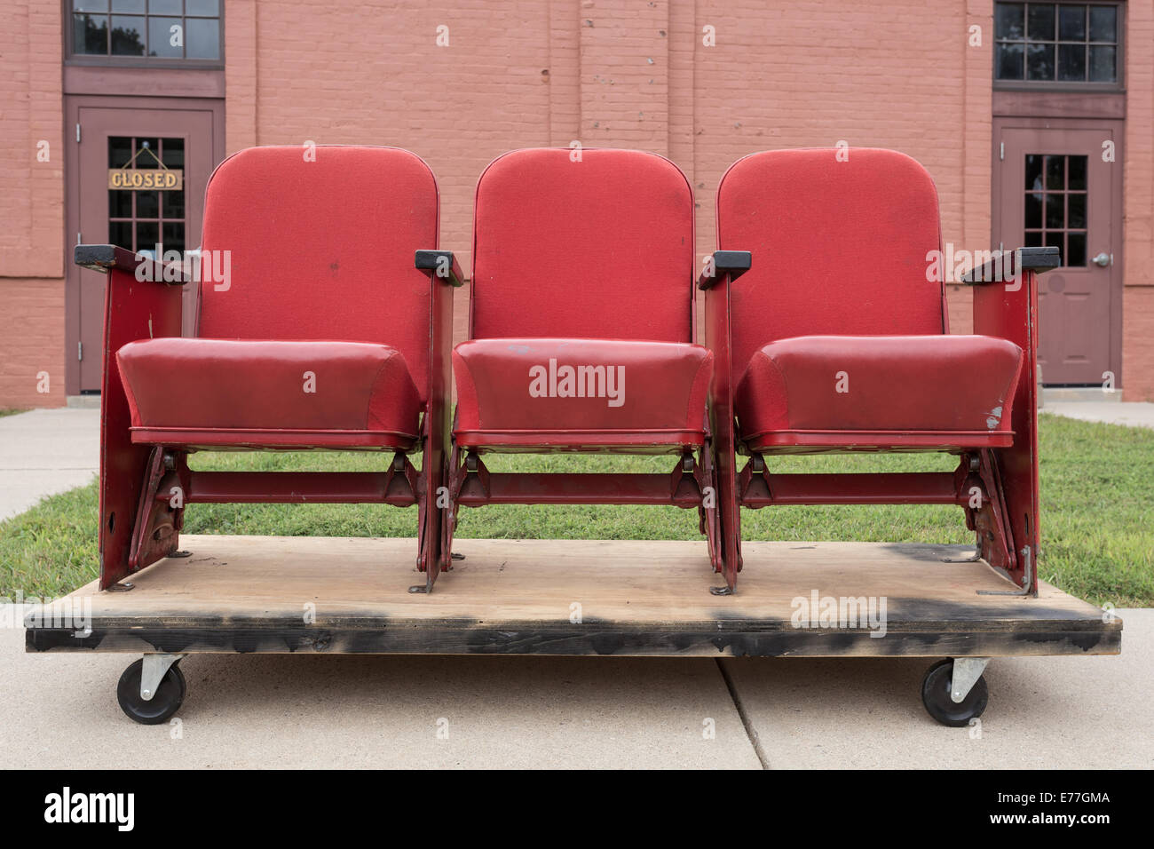 A section of three old movie theater seats on a pallet out side