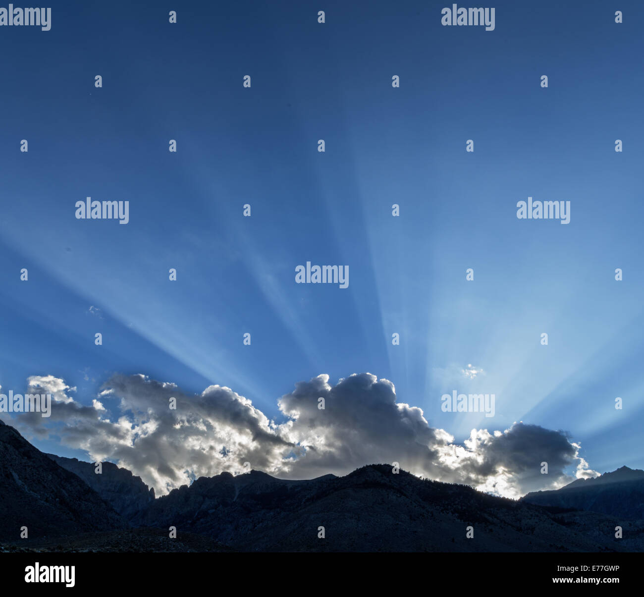 sunrays across a blue sky from behind a cloud over the Sierra Nevada Mountains and Taboose Pass Stock Photo