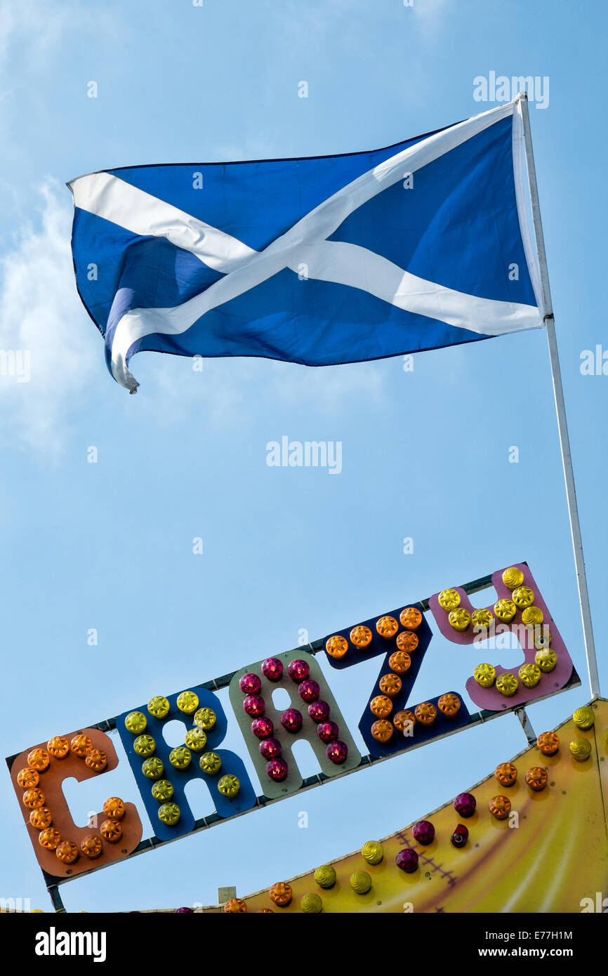 The Saltire, the Scottish national flag flying atop a flagpole above the word crazy written in multi coloured  fairground lights Stock Photo