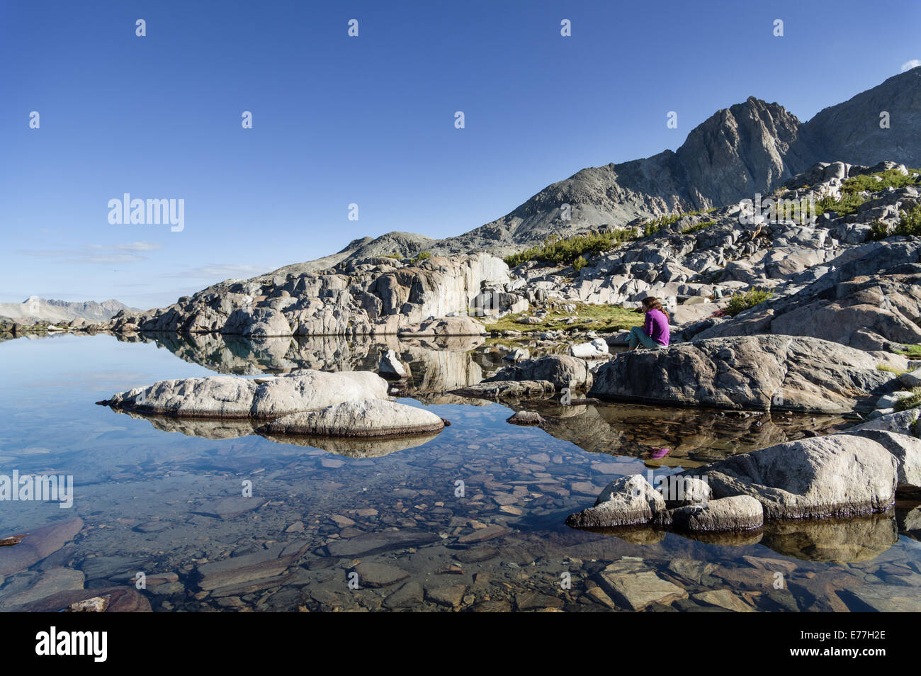 woman sitting on rock by still mountain lake in the morning Stock Photo