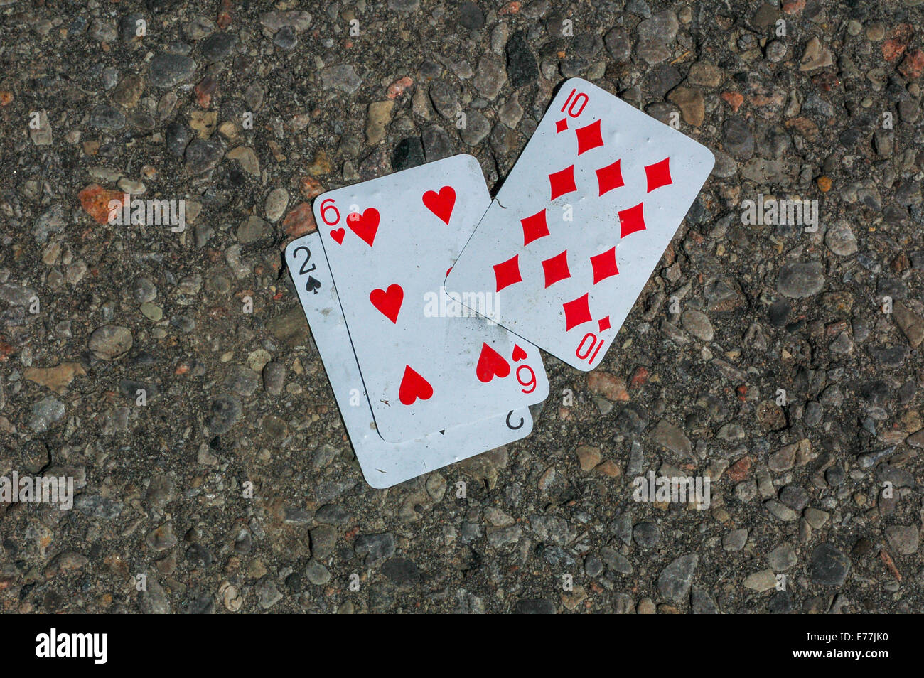 Three playing cards, two of spades, six of hearts and ten of diamonds found on an asphalt road. Stock Photo