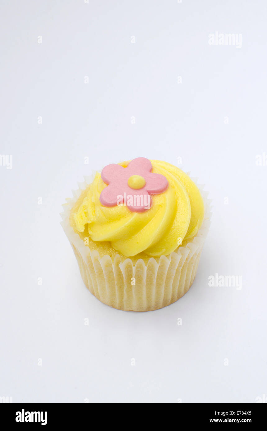 Mini cupcake with yellow icing and pink flower decoration on white