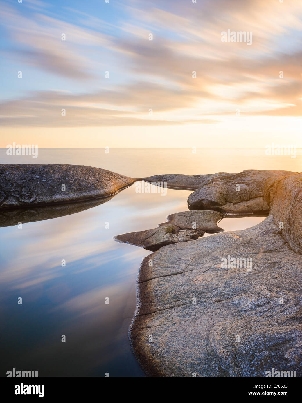 Smooth tide pool surrounded by rock at sunset Stock Photo