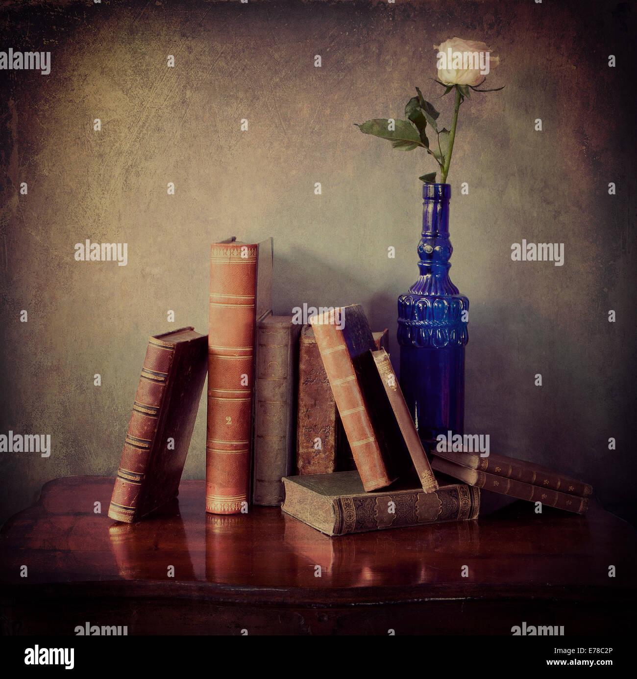 Interior still life, composition of antique books on a wooden table and a single pink rose in a blue  bottle with grunge texture Stock Photo